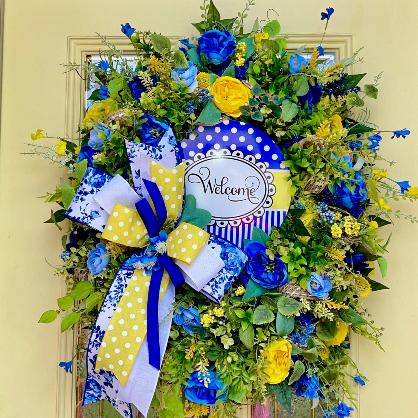 Decorative wreath with blue and yellow flowers and a 'Welcome' sign on a door.
