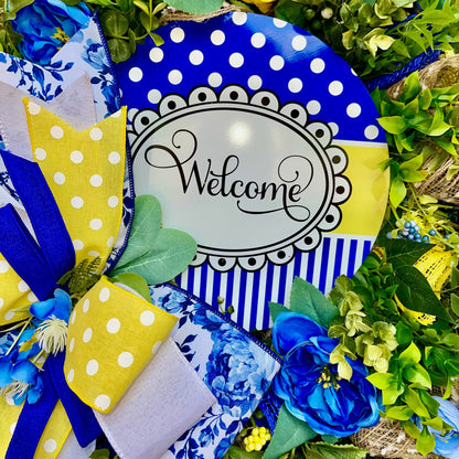 Decorative wreath with blue and yellow polka dot accents and a 'Welcome' sign, surrounded by greenery.