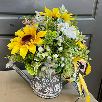 Floral arrangement with sunflowers and greenery in a decorative pot on a table.