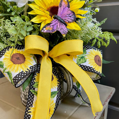 Decorative arrangement with sunflowers, a butterfly, and a yellow ribbon on a neutral background.
