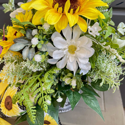 Bouquet of sunflowers and white flowers with greenery in a clear vase.