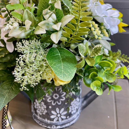 Artificial greenery in a decorative pot with floral elements on a blurred background