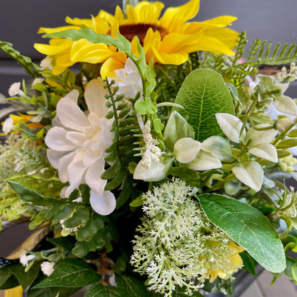 Bouquet of artificial flowers with sunflowers, white flowers, and green leaves.