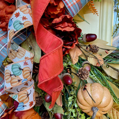 Decorative wreath with autumn-themed ribbons, pumpkins, and leaves.