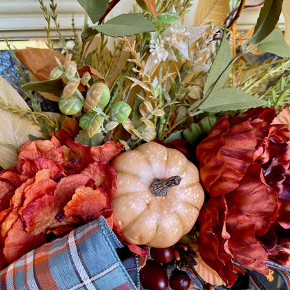 Decorative wreath with pumpkins, flowers, and plaid fabric on a table.