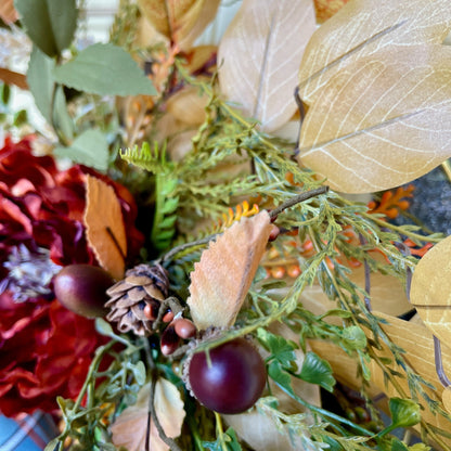 Decorative wreath with artificial leaves, berries, and pinecones on a blurred background