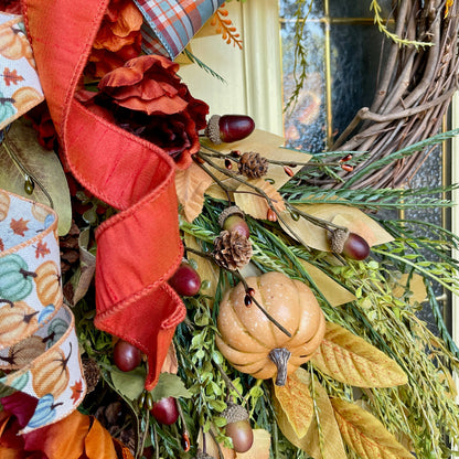 Decorative autumn wreath with pumpkins, ribbons, and leaves on a door.