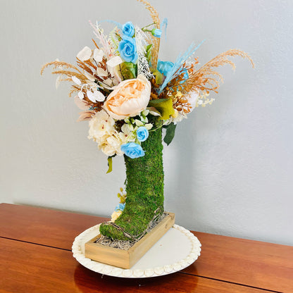 Decorative floral arrangement in a moss-covered boot on a wooden surface with a plain background