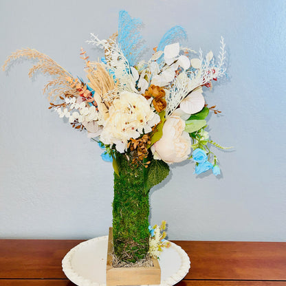 Floral arrangement with a moss-covered boot on a wooden surface against a light blue wall.