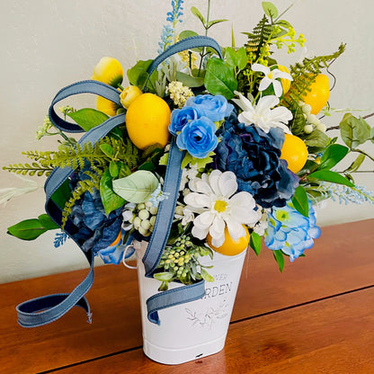 Bouquet of flowers with blue, yellow, and white flowers in a white container on a wooden surface.