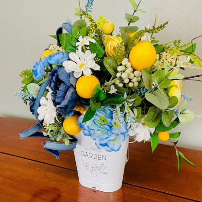 Bouquet with blue, yellow, and white flowers in a white container on a wooden surface.