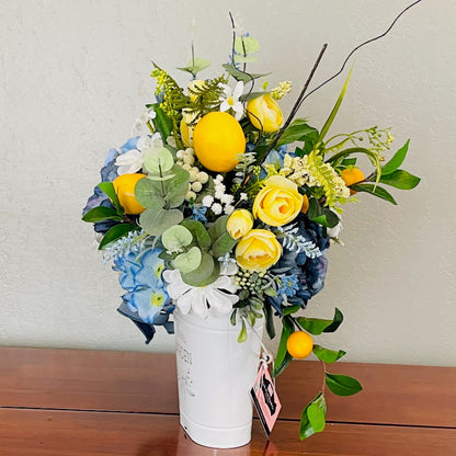 Bouquet of flowers with yellow roses and blue hydrangeas in a white vase on a wooden surface.