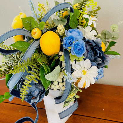 Bouquet with lemons, blue and white flowers, and greenery on a wooden surface.