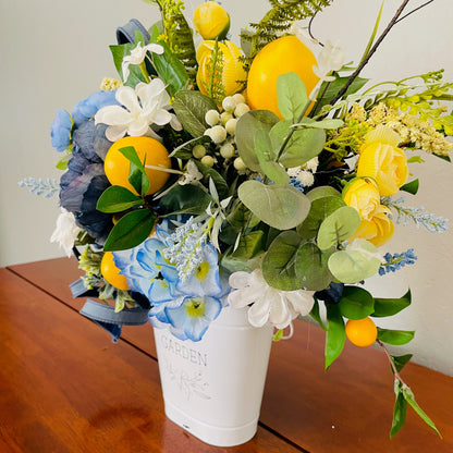 Bouquet of flowers with lemons and blue hydrangeas in a white vase on a wooden surface.
