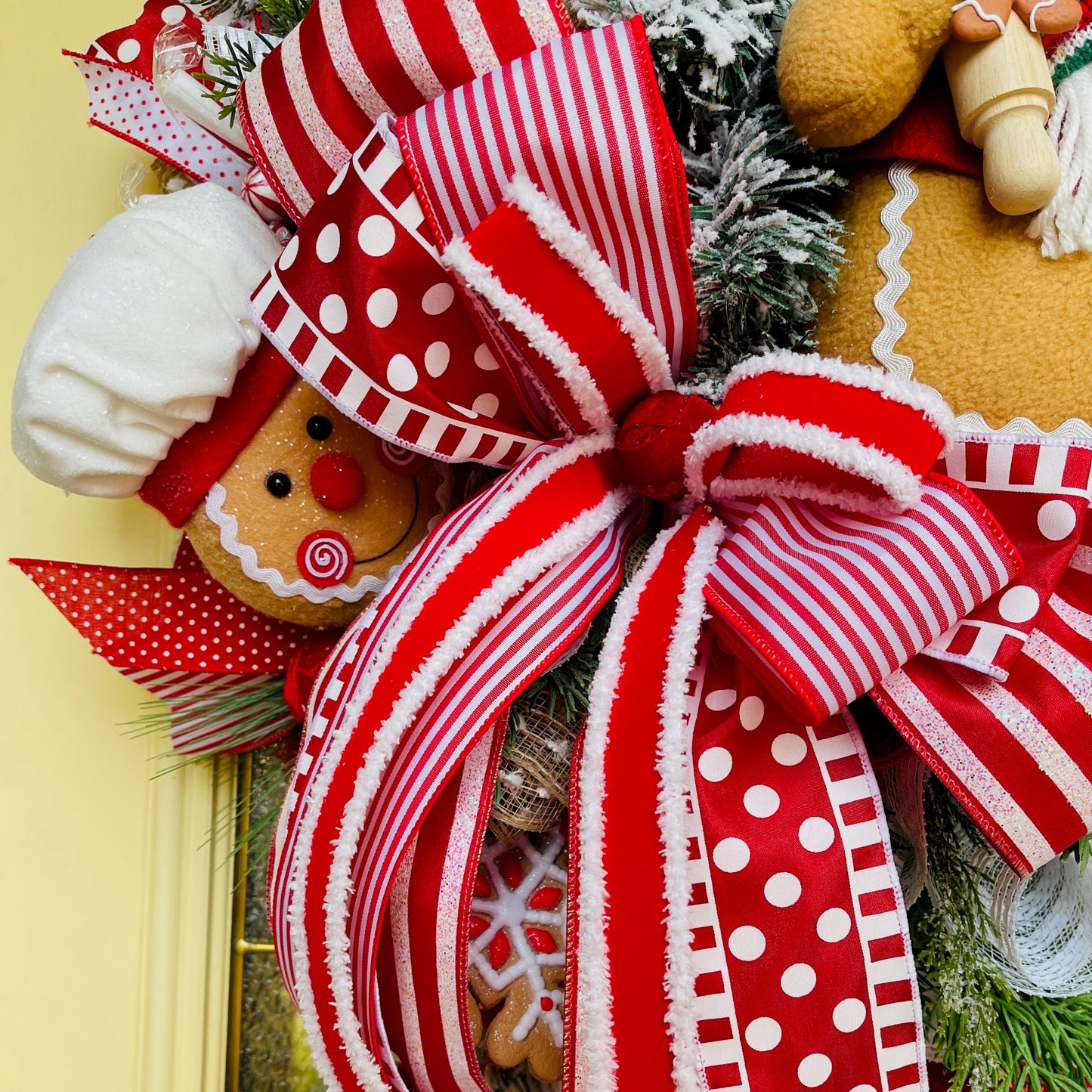 Decorative wreath with a large red and white bow, gingerbread men, and Christmas tree on a yellow background.