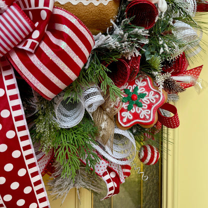 Decorative Christmas wreath with red and white ribbons, greenery, and a gingerbread cookie design on a yellow door.