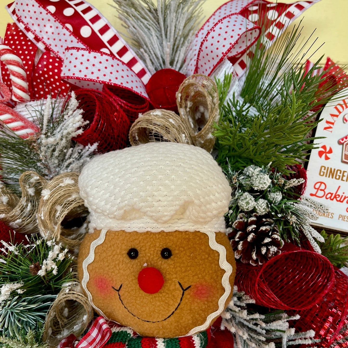 Decorative Christmas wreath with a gingerbread man design, surrounded by greenery and ribbons.