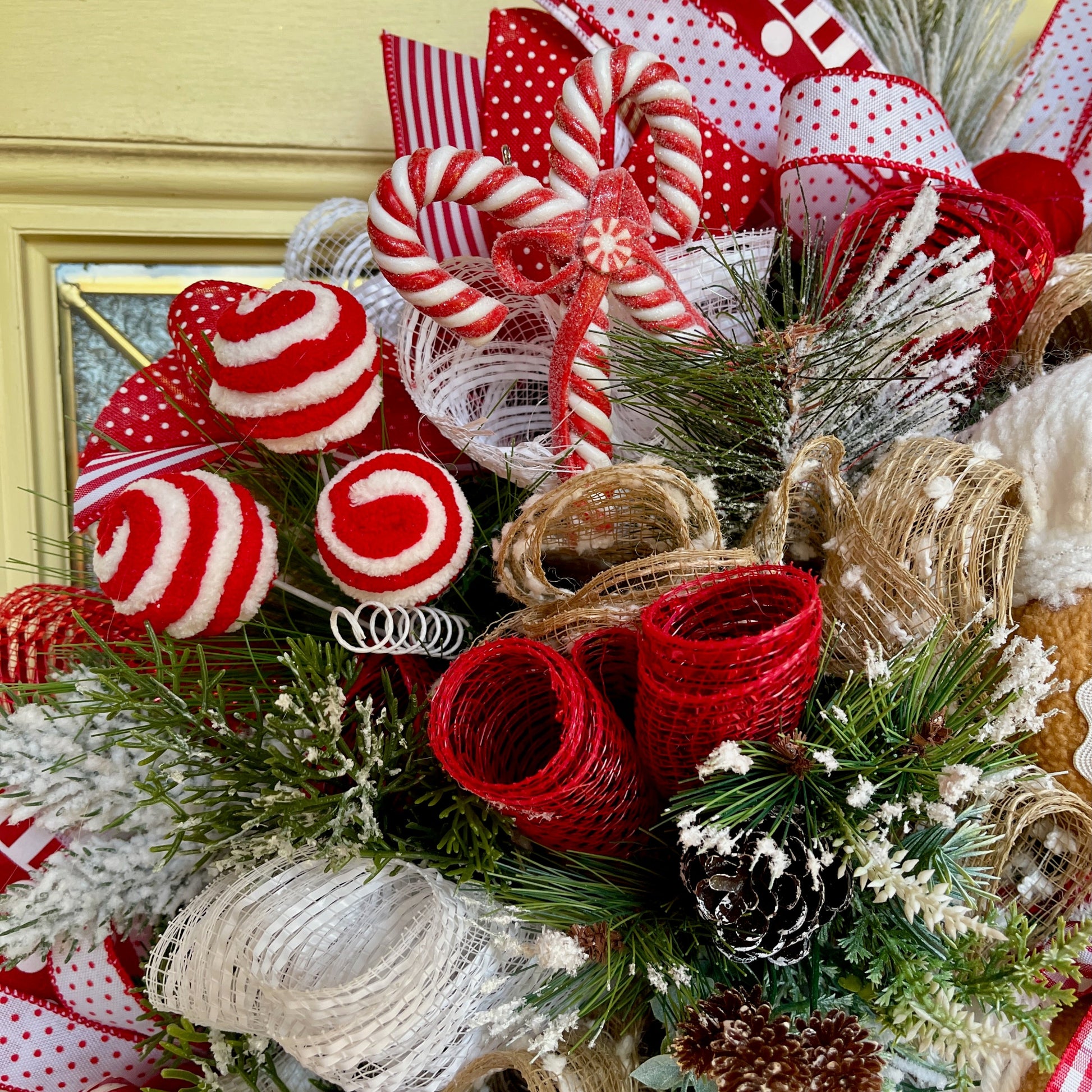 Decorative Christmas wreath with red and white candy cane ornaments, ribbons, and pine cones.