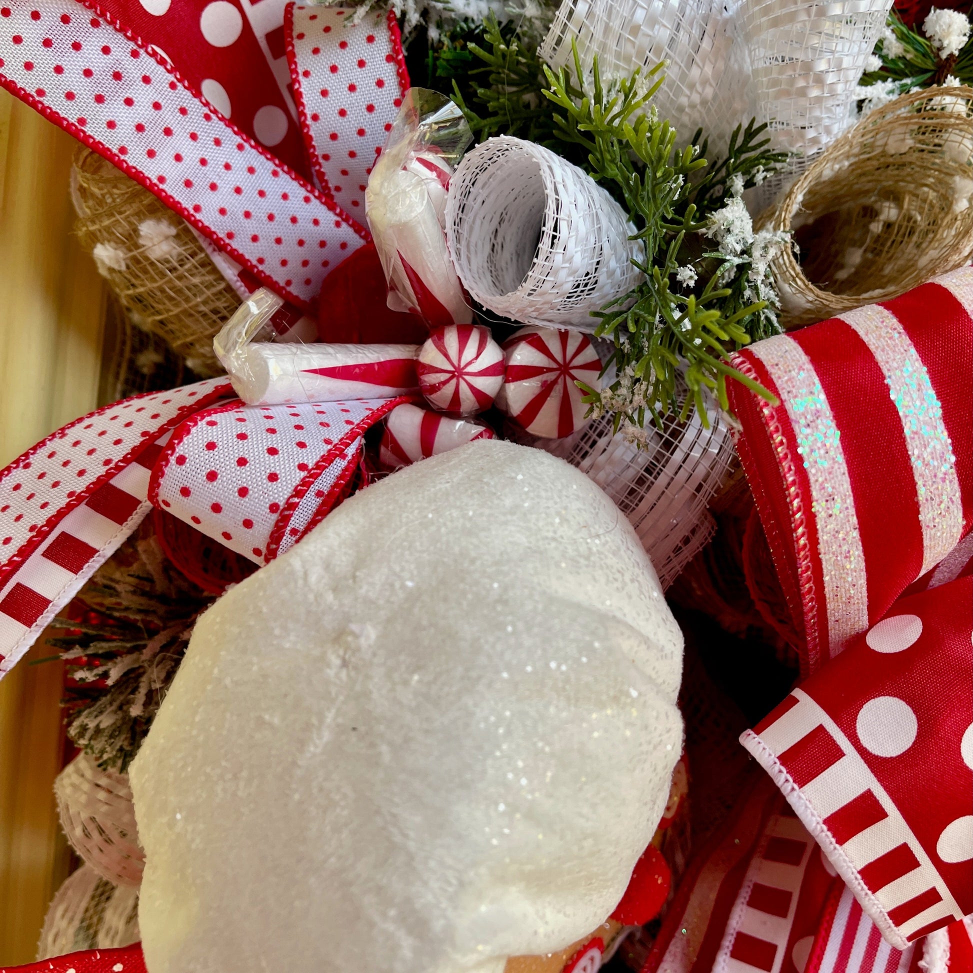 Decorative wreath with red and white ribbons, greenery, and a snowman ornament.