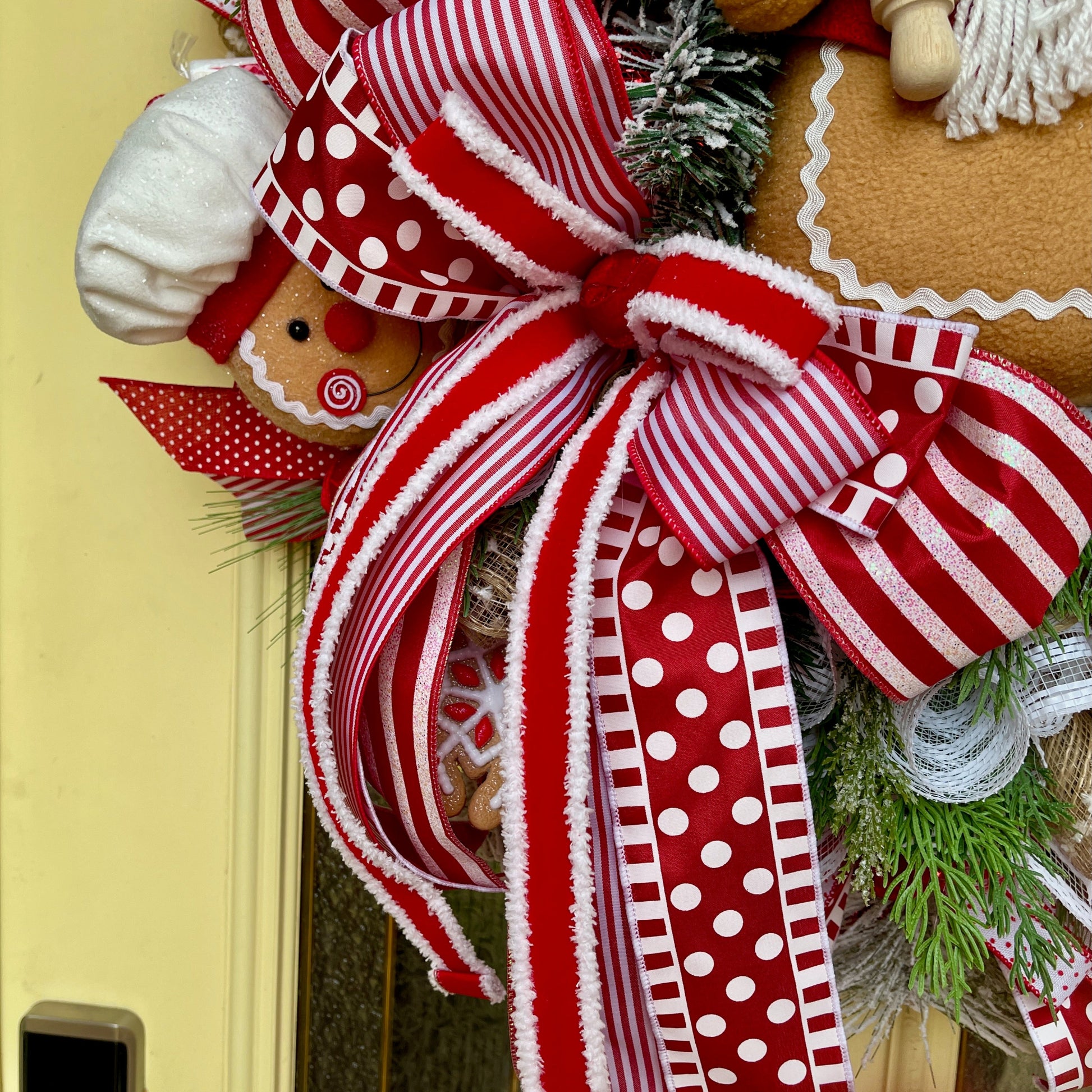 Decorative wreath with red and white ribbons and gingerbread man on a yellow door.