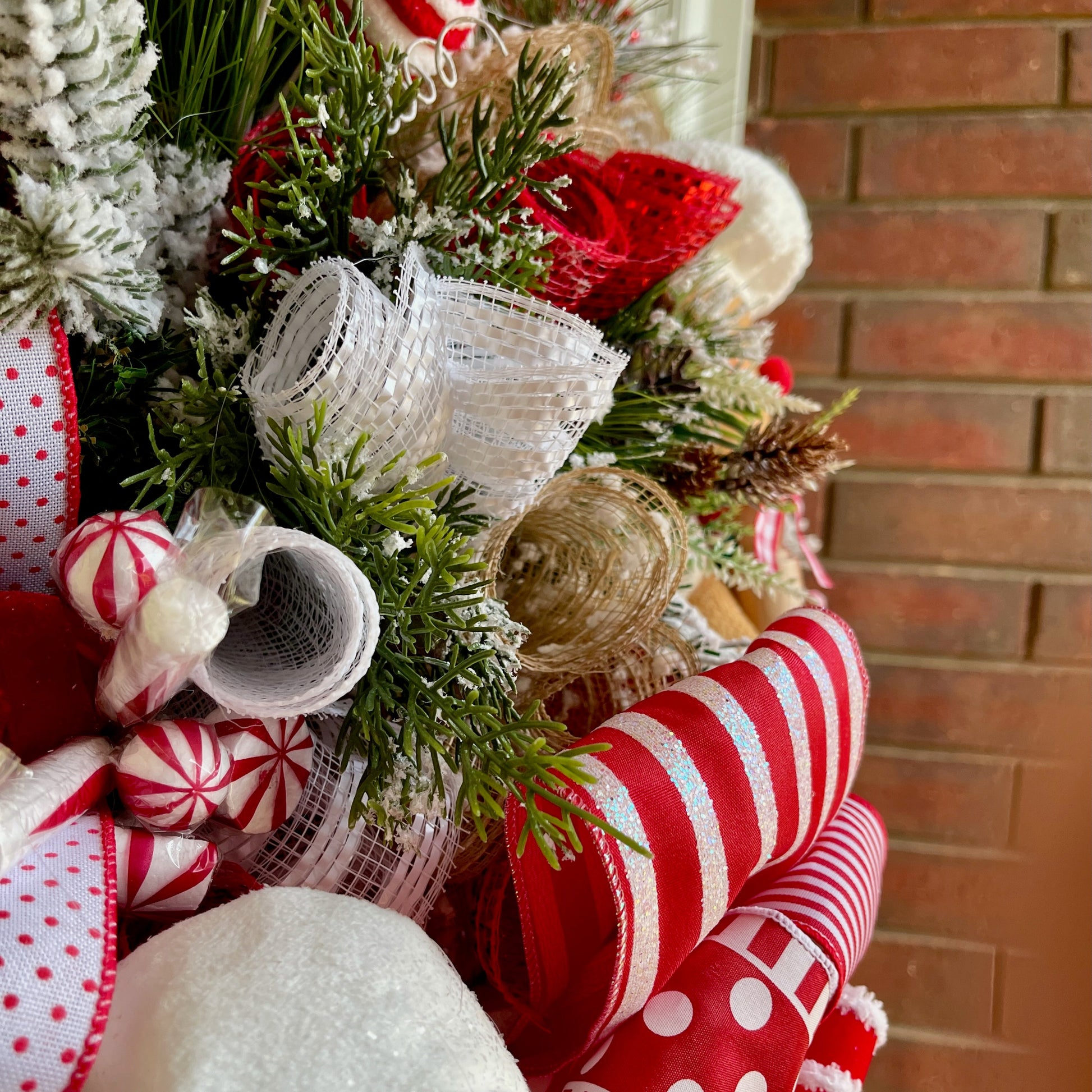 Close-up of a Christmas wreath with red, white, and green decorations against a brick wall.