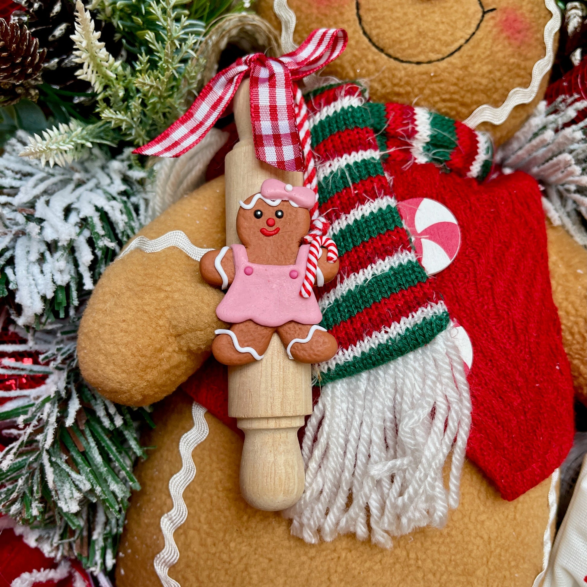 Decorative gingerbread man with a scarf and candy cane, surrounded by Christmas decorations.