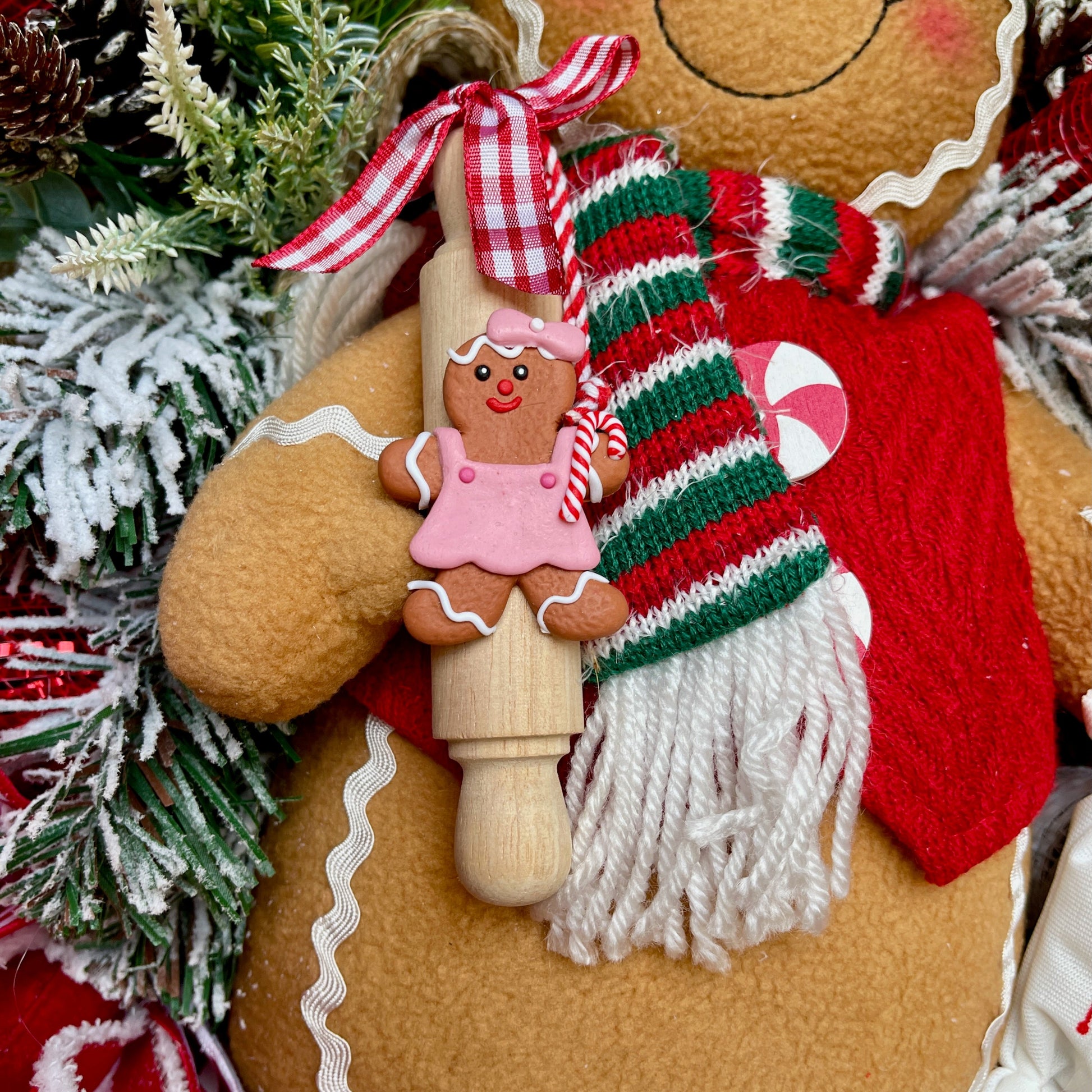 Decorative gingerbread man with a wooden candy cane and gingerbread girl ornament, surrounded by Christmas decorations.