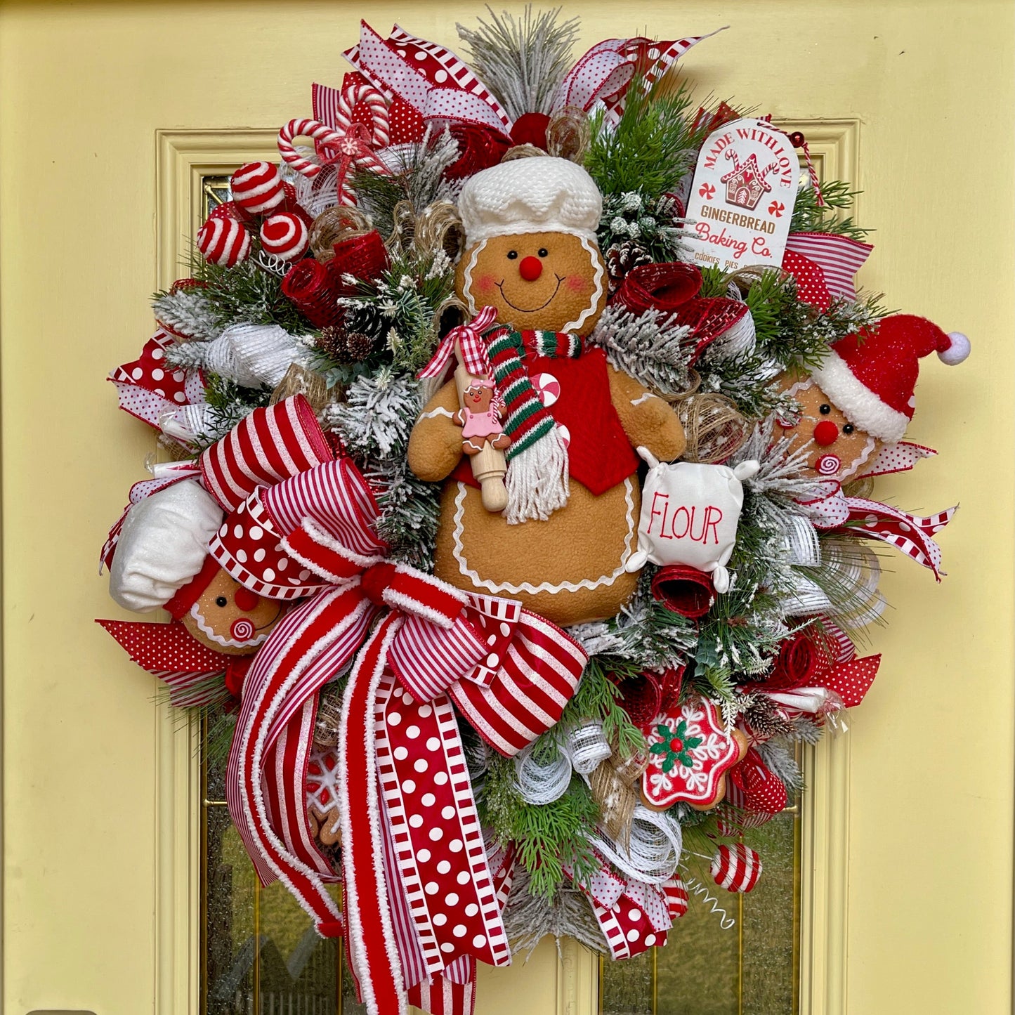 Decorative Christmas wreath with gingerbread man and red ribbons on a yellow door.