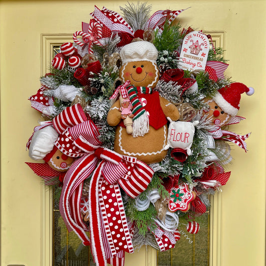 Decorative Christmas wreath with gingerbread man and red ribbons on a yellow door.