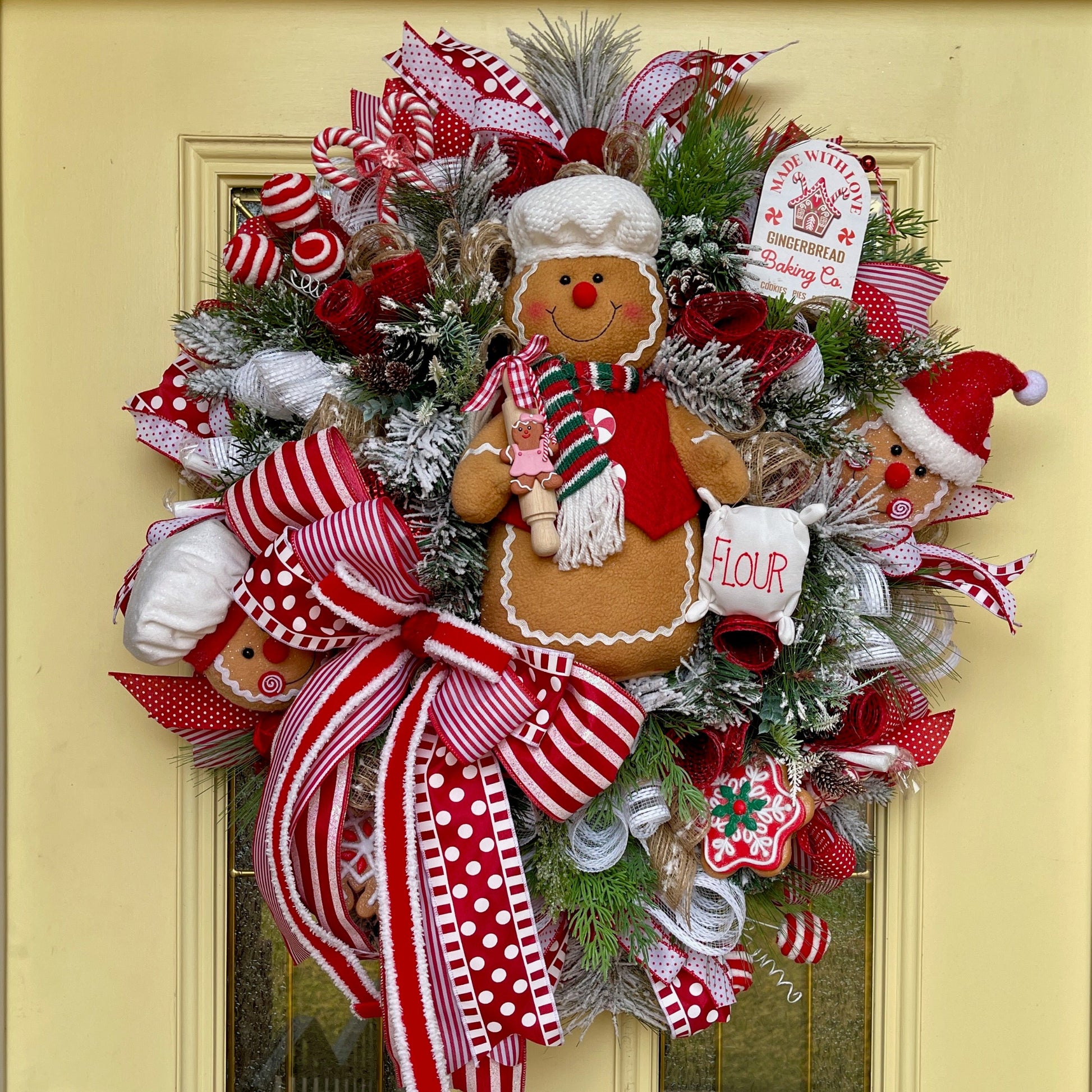 Christmas wreath with gingerbread man, ribbons, and decorative elements on a yellow door.