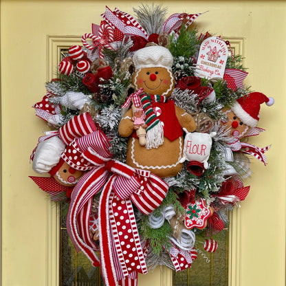 Christmas wreath with gingerbread man, ribbons, and decorative elements on a yellow door.