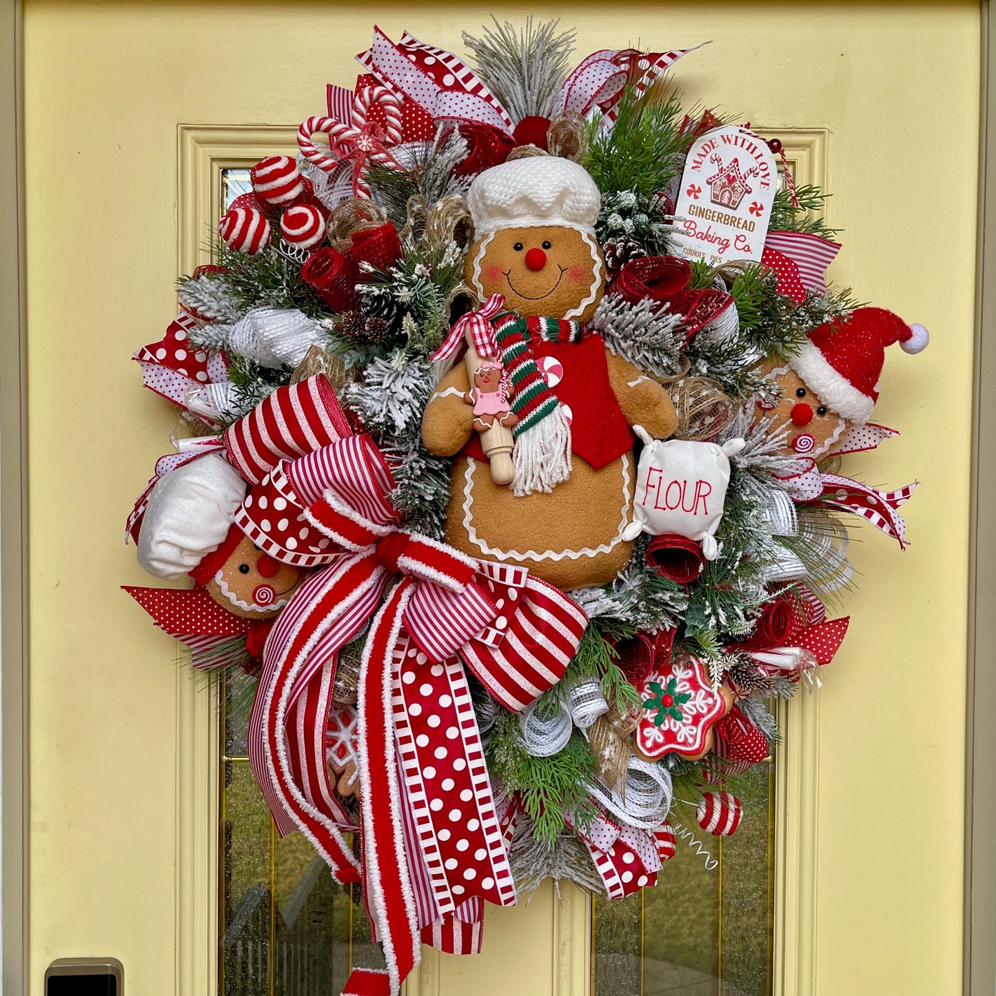Decorative Christmas wreath with gingerbread man and candy cane on a yellow door.
