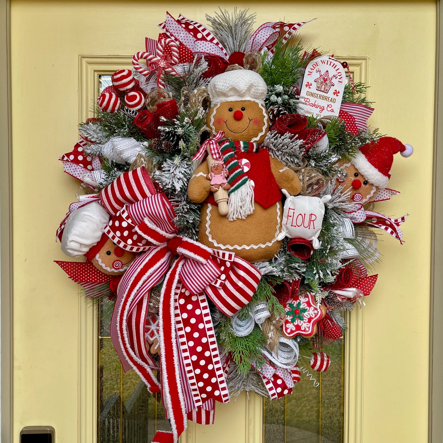 Decorative Christmas wreath with gingerbread man and candy cane on a yellow door.